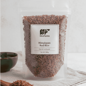 A standing pouch of HimFarms Himalayan Red Rice next to a bowl of cooked red rice and a wooden spoon.